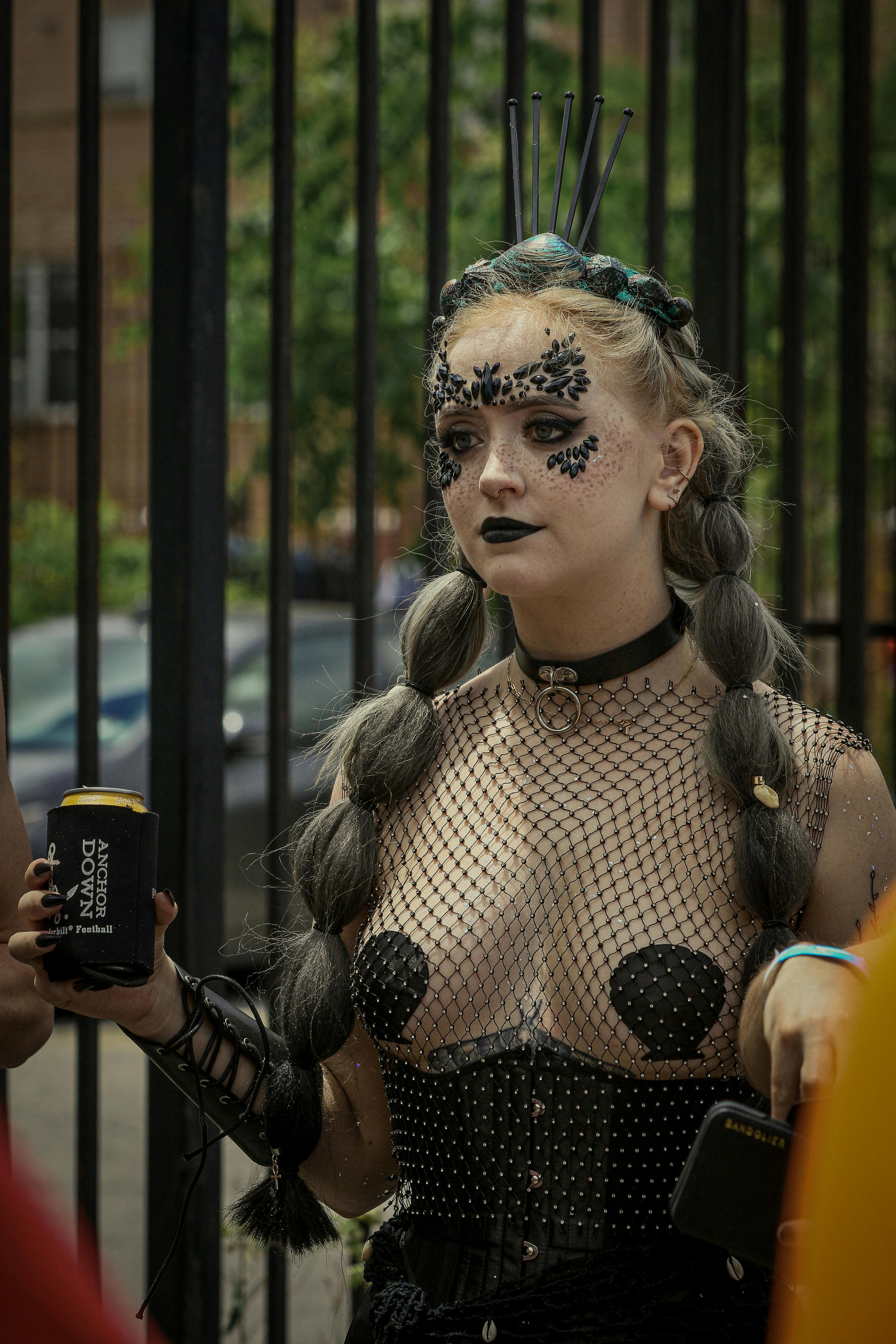 Woman with elaborate makeup and costume holding a beverage can outdoors.