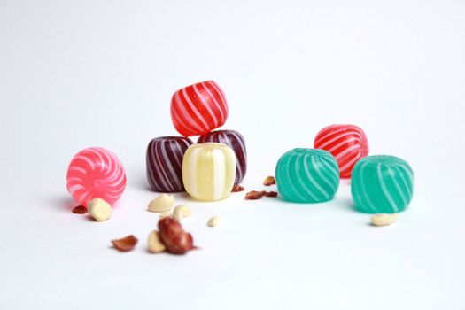 Vibrant striped candies scattered with nuts on a plain white background, showcasing vivid colors.