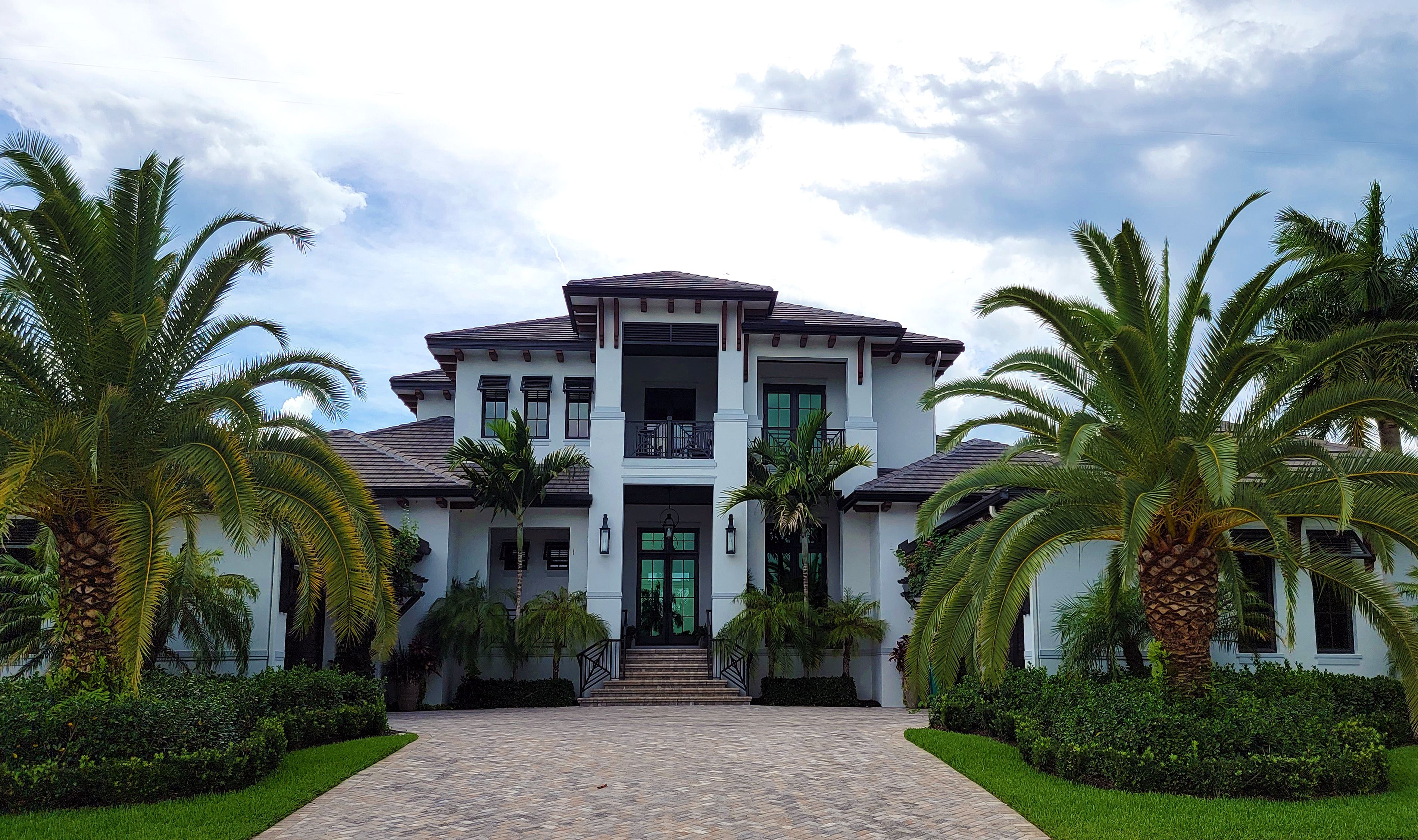 High-end South Florida mansion with a manicured lawn and mature royal palms framing the entrance