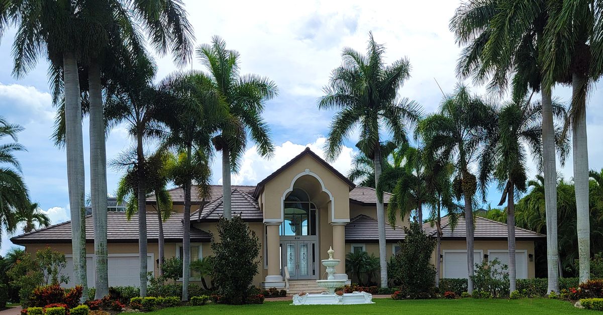 Stunning mansion exterior surrounded by palm trees, showcasing a tropical paradise setting.