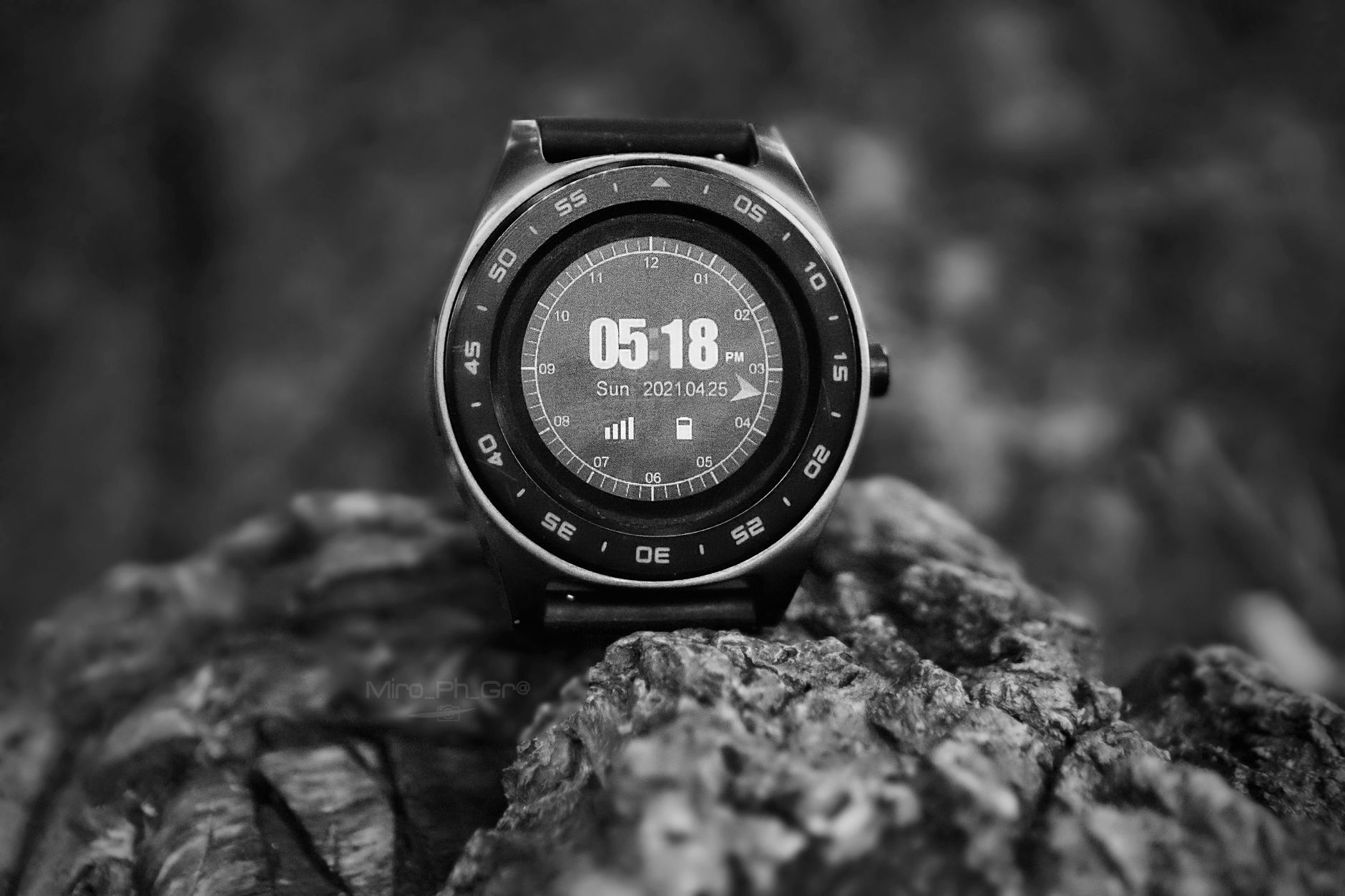 Close-up of a stylish smartwatch in grayscale, showcasing time and date on rocky background.
