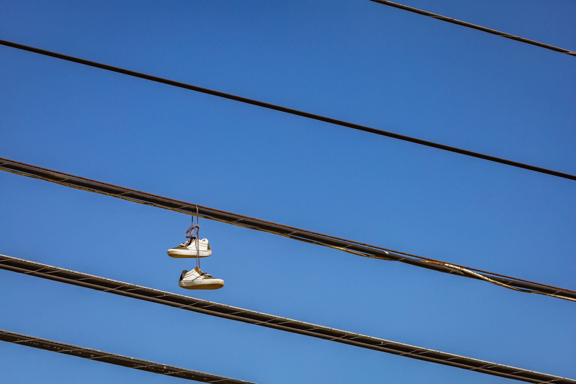 Pair of sneakers hanging on electric wires with a clear blue sky background.