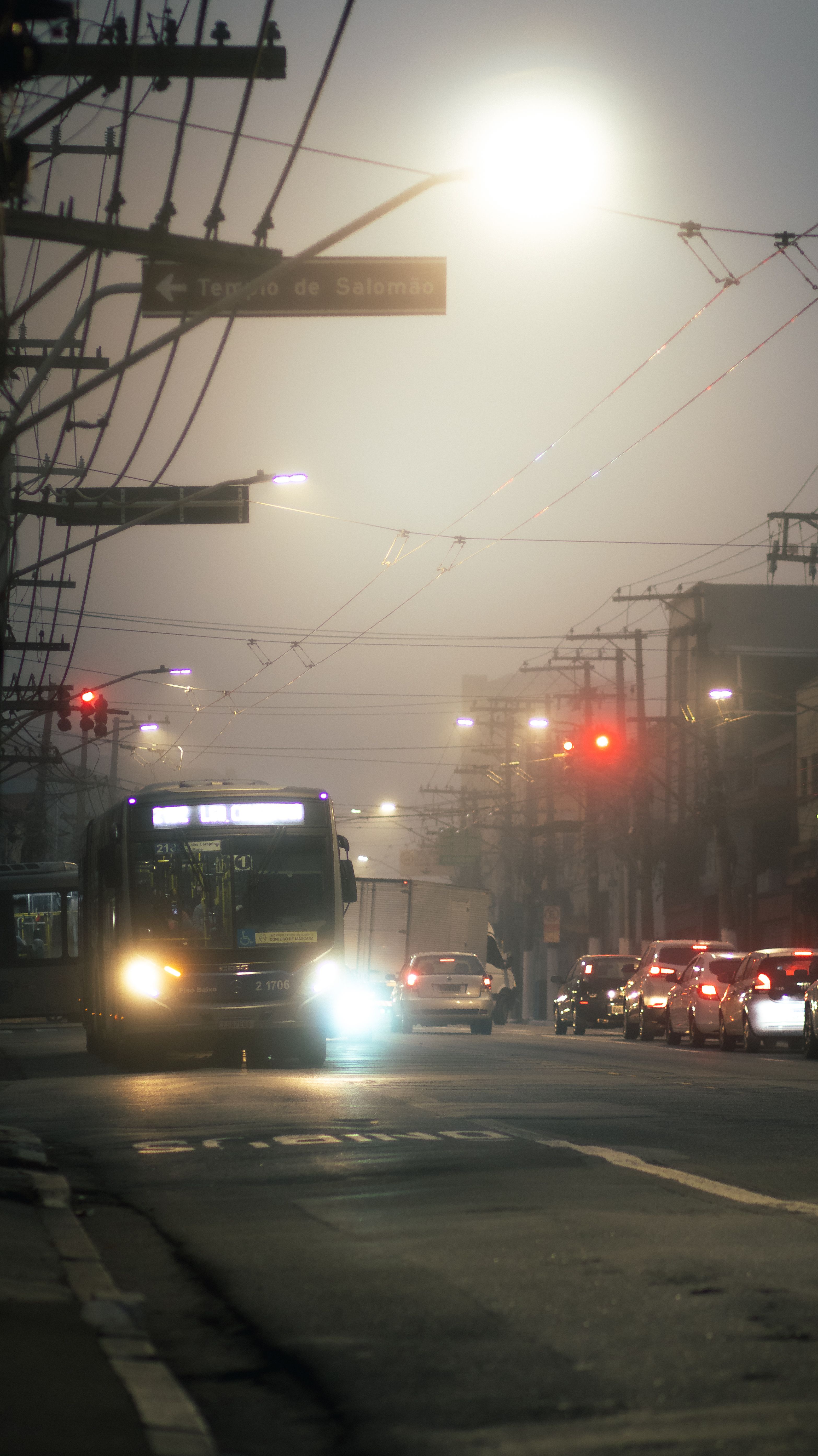 Nighttime street scene with bus and cars in a foggy urban setting, highlighting city life.