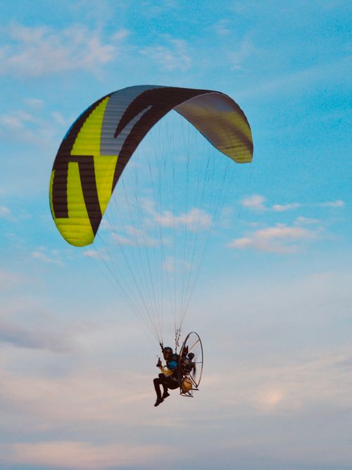 Free A thrilling paramotor flight capturing the essence of adventure against a bright blue sky. Stock Photo