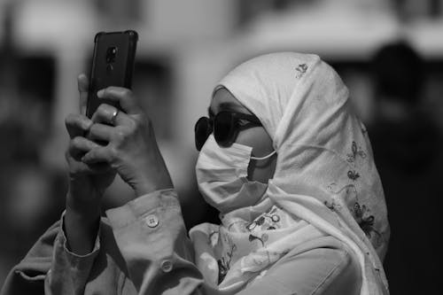 Grayscale Photo of a Woman in White Hijab Holding a Smartphone