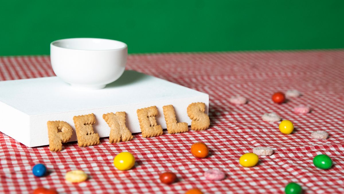 Close-up of alphabet cookies spelling PEXELS with colorful candies on a checkered tablecloth.