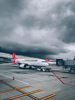 A Turkish Airlines aircraft parked at a runway under a stormy sky, ready for boarding.