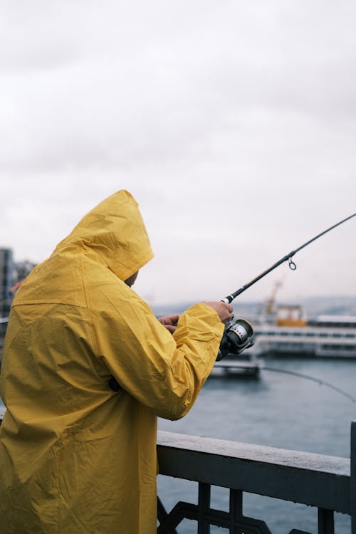 一個穿著黃色雨衣的漁夫在橋上釣魚