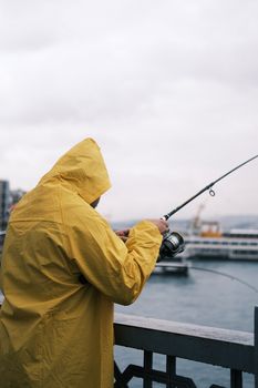 Person in yellow raincoat fishing by the waterfront in Istanbul, Turkey.