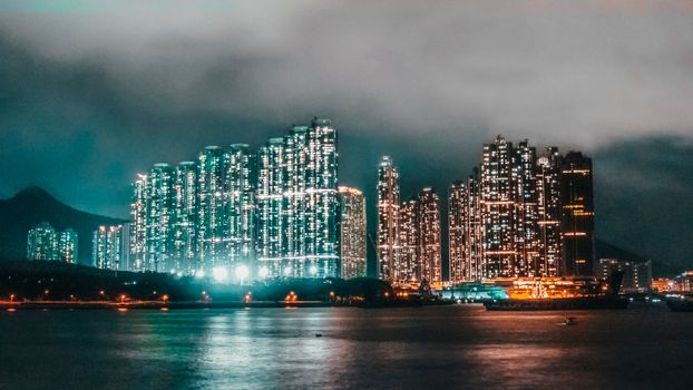 A vibrant nighttime cityscape featuring illuminated skyscrapers reflected on calm waters.
