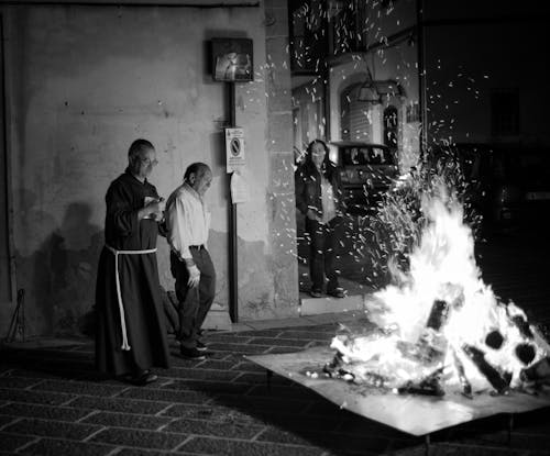 Grayscale Photo of People Standing Beside the Bonfire