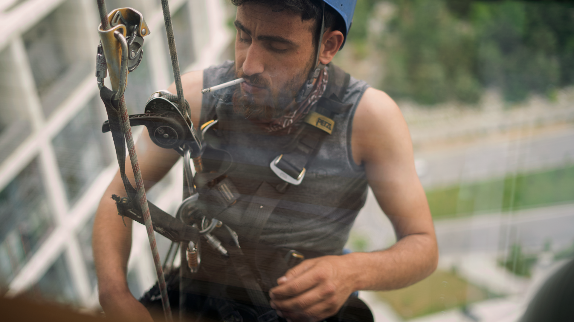 Worker suspended on ropes with helmet, accessing high-rise building facade.