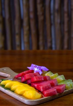 Colorful tropical fruit slices on a wooden board with a purple flower garnish, ideal for healthy eating visuals.