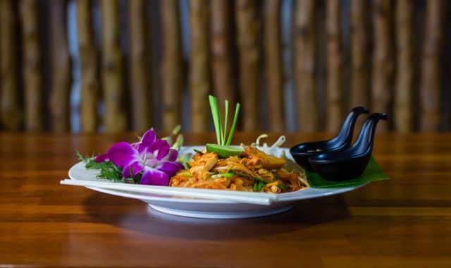 Close-up of a traditional Thai Pad Thai dish with vibrant floral garnishes, exuding a tasty and appetizing look.