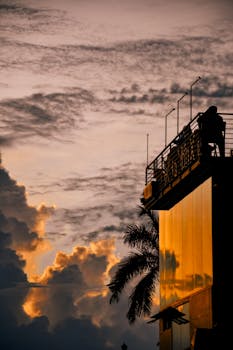Silhouette of a person on a rooftop against a dramatic sunset and cloudscape.