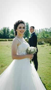 Beautiful bride smiling outdoors in her wedding gown holding a bridal bouquet.