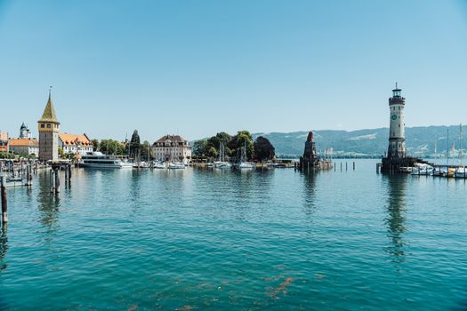 Panoramic view of Lindau harbor with lighthouse, boats, and buildings against blue sky.