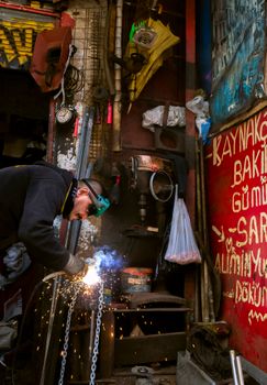 A welder working in a workshop full of tools