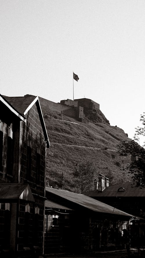 Black and White Photo of a Hill with a Flag, and Houses in Foreground