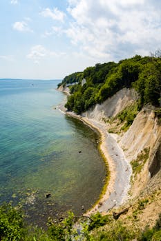 A scenic aerial view of white chalk cliffs and lush greenery along a calm blue sea coastline.
