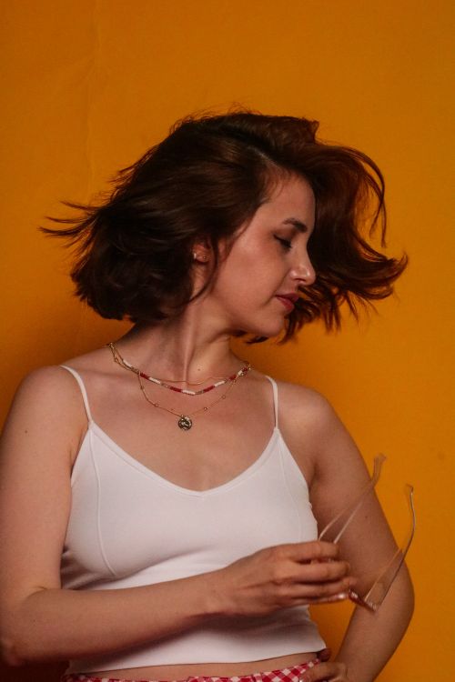 Free Stylish portrait of a woman with a hair flip against a vibrant orange background, embodying modern fashion. Stock Photo