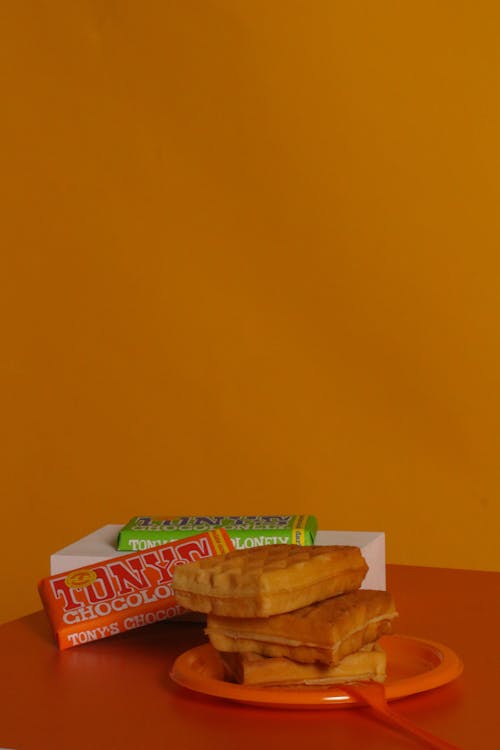 A Plate of Waffles Beside Bars of Chocolates on an Orange Surface