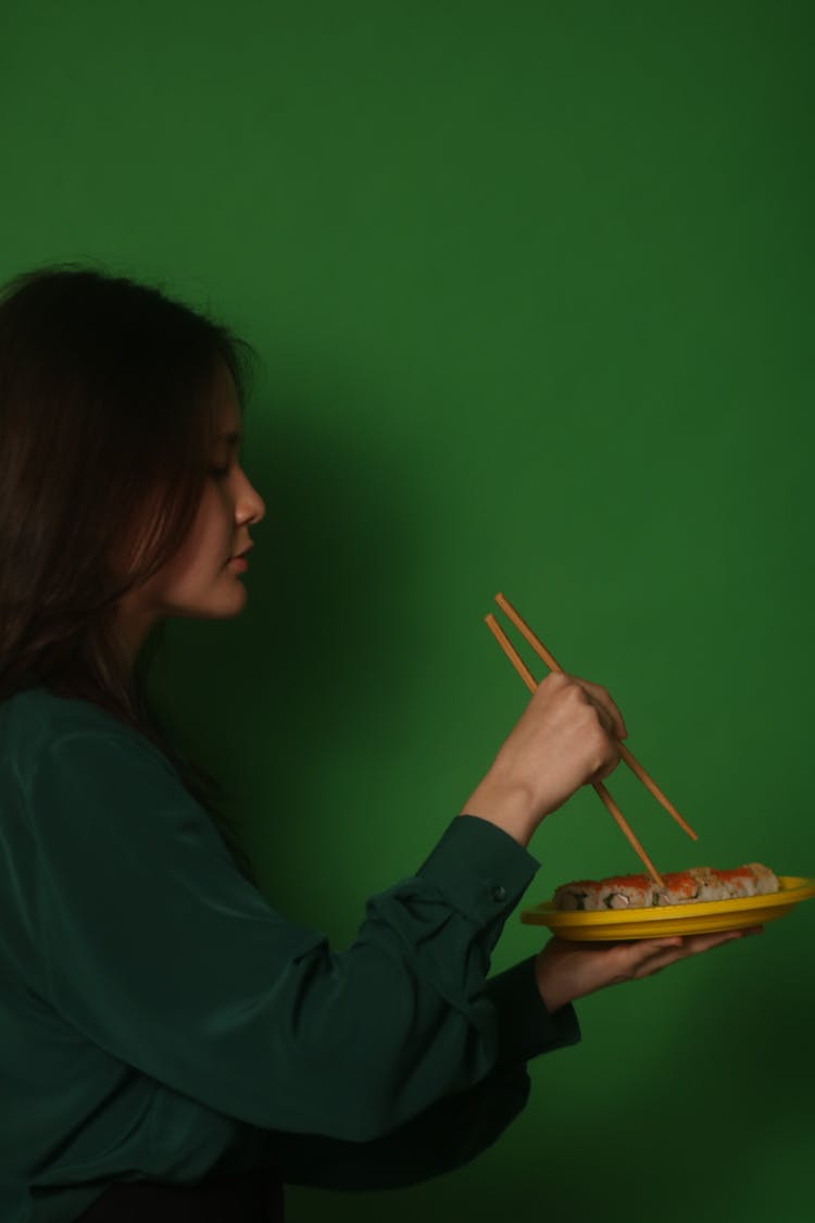 Side View Of A Woman Getting Sushi Rolls With Chopsticks