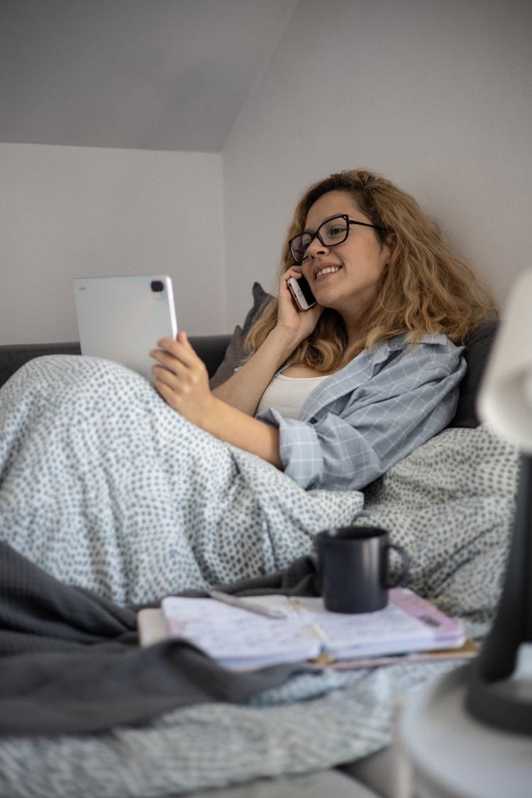 A Woman Talking On The Phone While Holding A Tablet