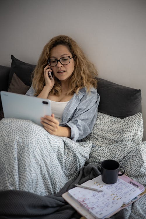 Free A Woman Sitting on Bed While Talking on the Phone Stock Photo