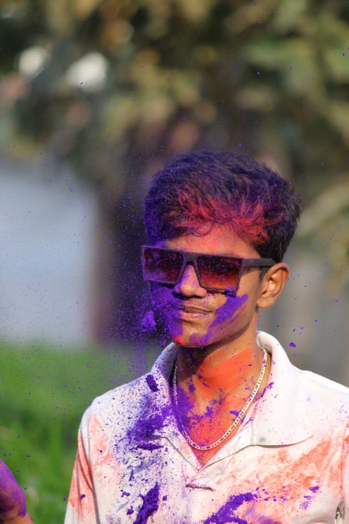 Free Adult male joyfully celebrating Holi festival with bright colored powders and sunglasses. Stock Photo