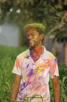 A teenager covered in vibrant powders celebrating Holi outdoors.