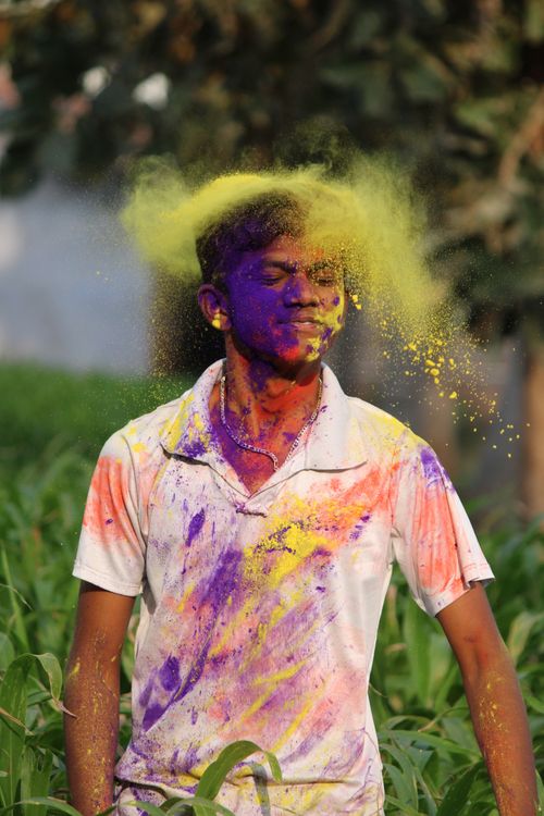 Free Man enjoying Holi festival with vibrant colors powdered over him outdoors. Stock Photo