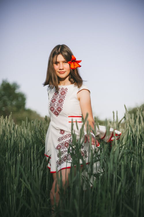 Beautiful Woman with Red Flower on Her Ear Walking on Green Wheat Field