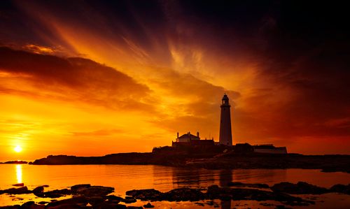 Free Dramatic sunset over a scenic lighthouse by the ocean, casting a striking silhouette. Stock Photo