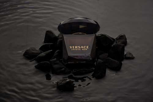 Free Elegant product shot of Versace Crystal Noir perfume on black stones. Stock Photo