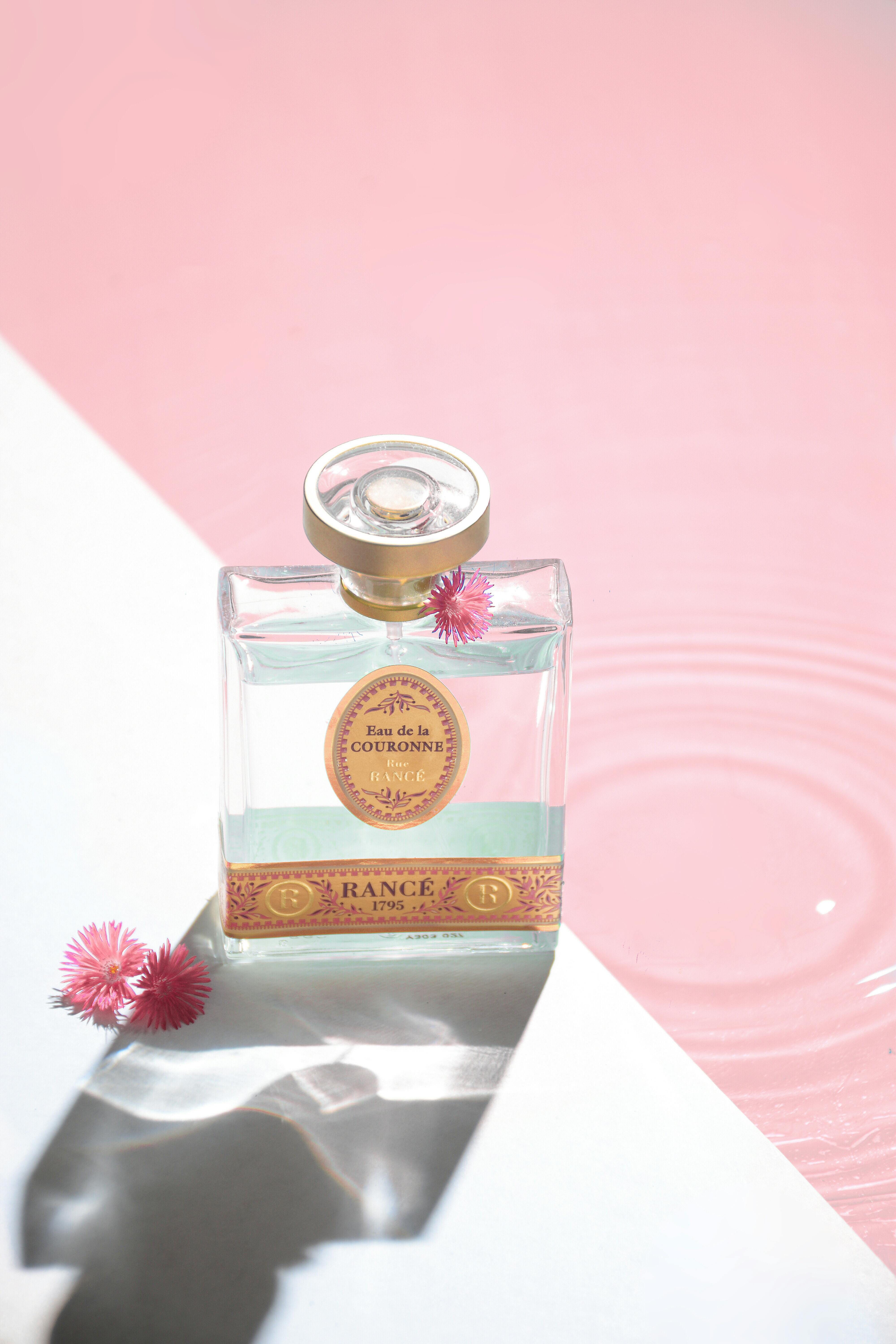 Glass perfume bottle with pink flowers and soft reflections in sunlight.
