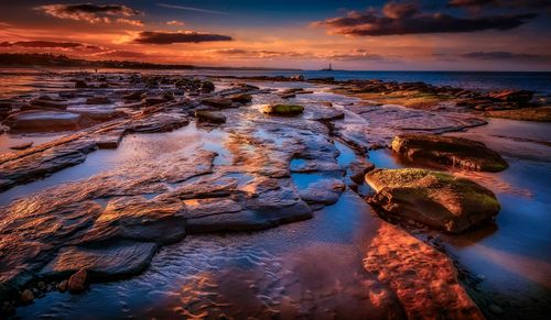 Free Dramatic sunset over rocky coastline with vibrant sky and sea reflection. Stock Photo