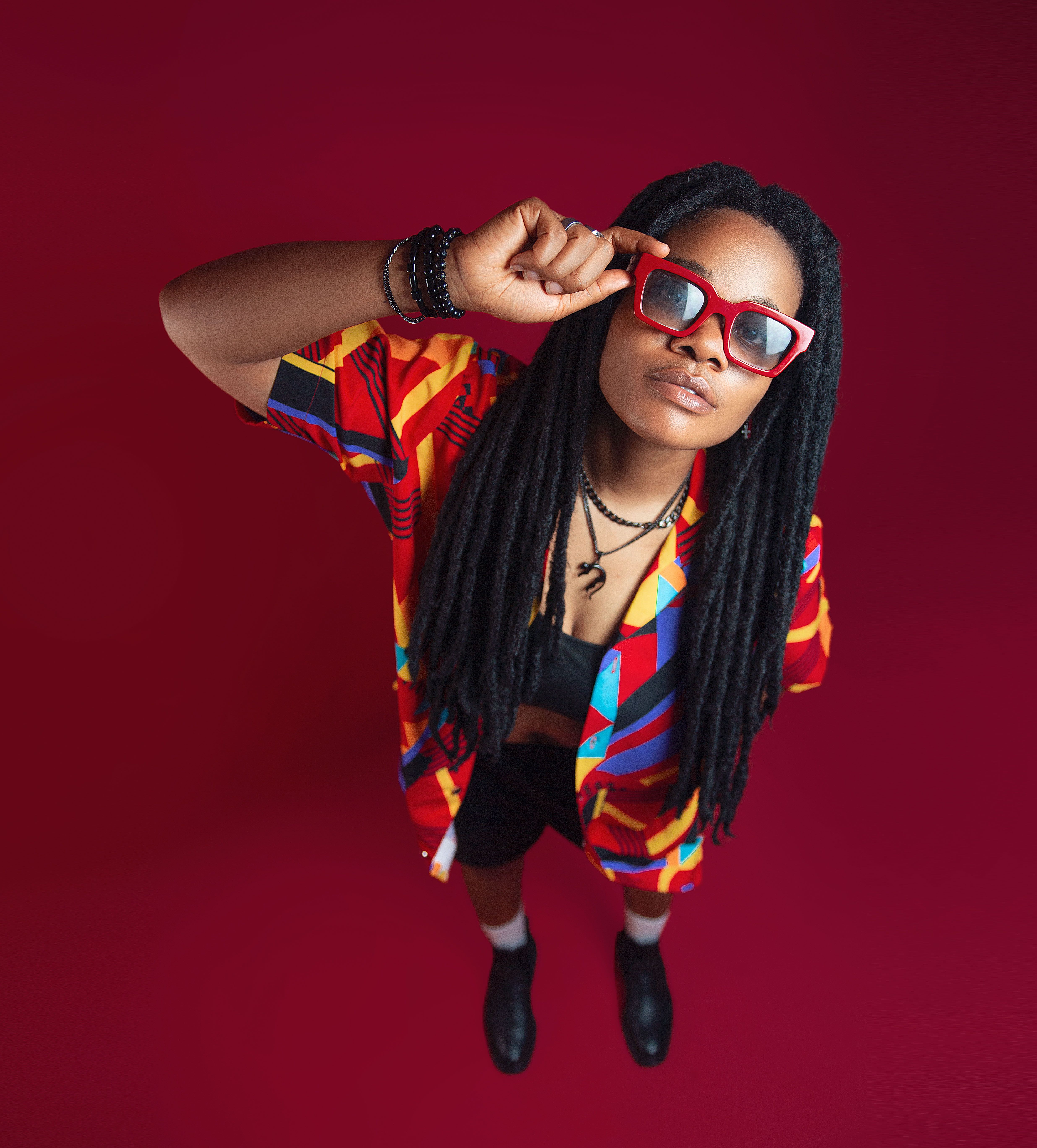Colorful portrait of an adult with long hair and vibrant clothing, set against a striking red background.