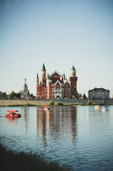 Majestic castle with green rooftops reflected in a tranquil lake under a clear sky.