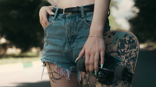 Free Person holding a skateboard with denim shorts, showcasing urban lifestyle. Stock Photo