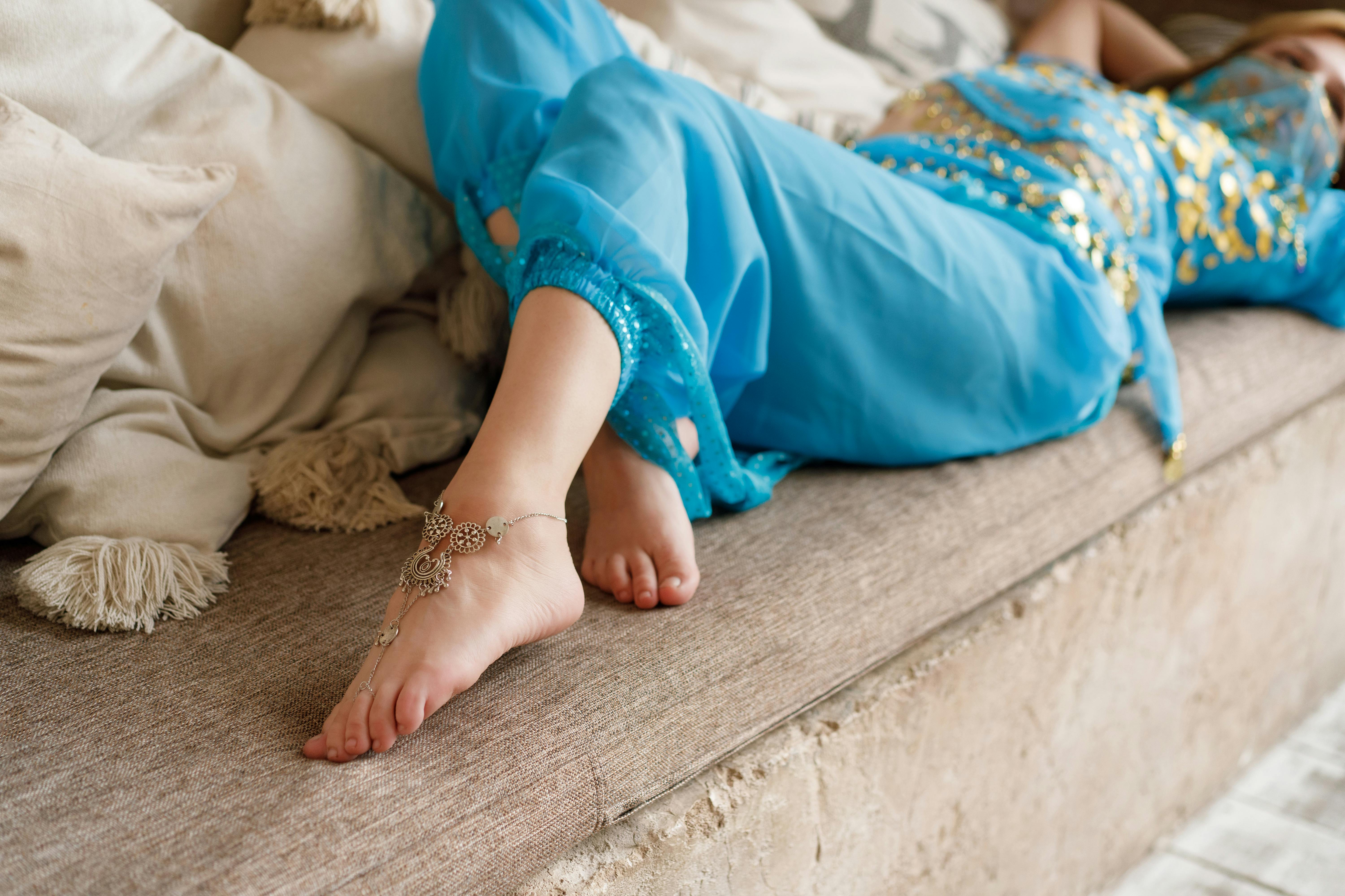 A woman lounges on a sofa, wearing a traditional blue dress with an intricate anklet.