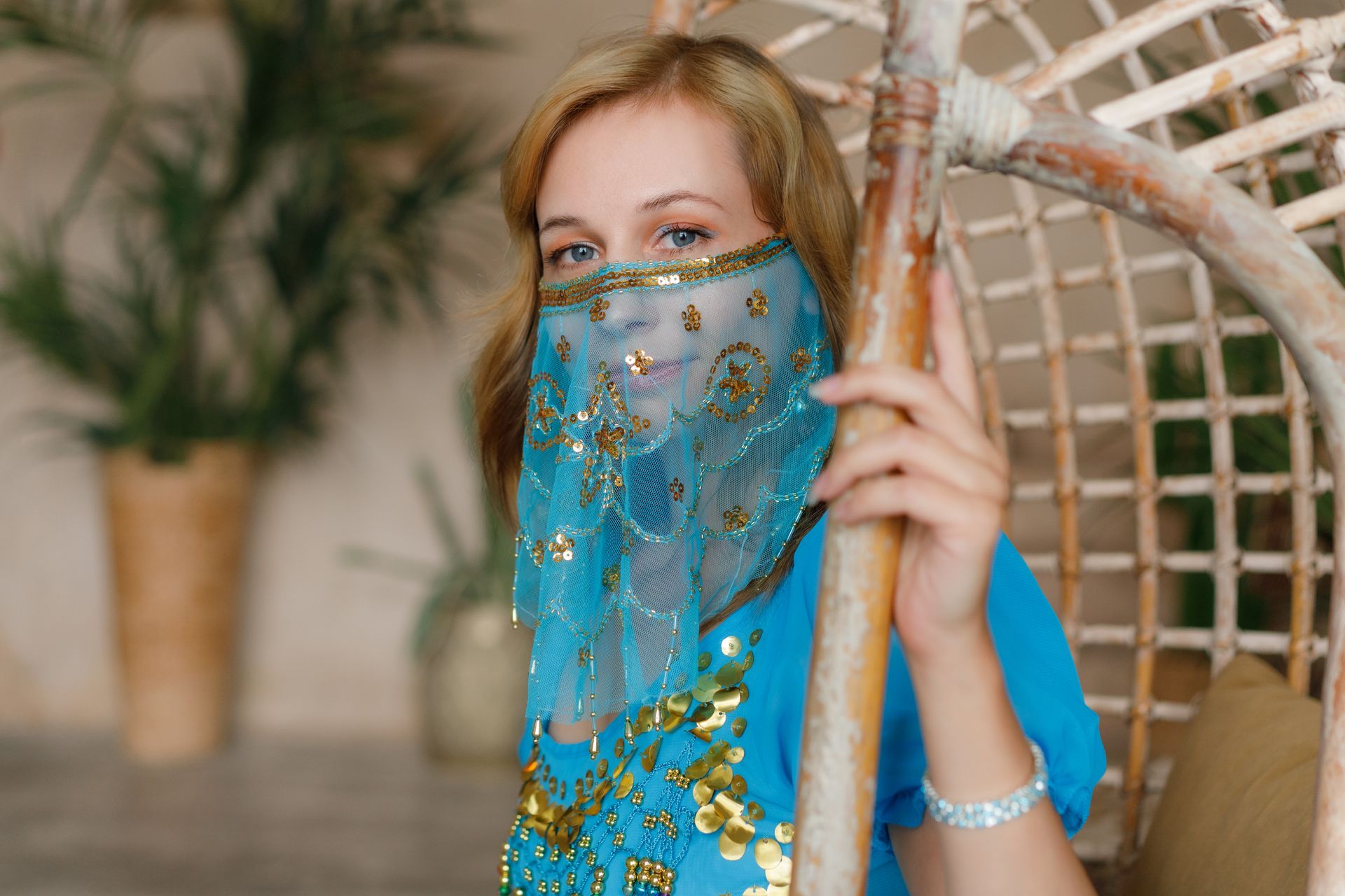 Close-up of a woman in oriental clothing wearing a beautifully decorated blue face veil indoors.