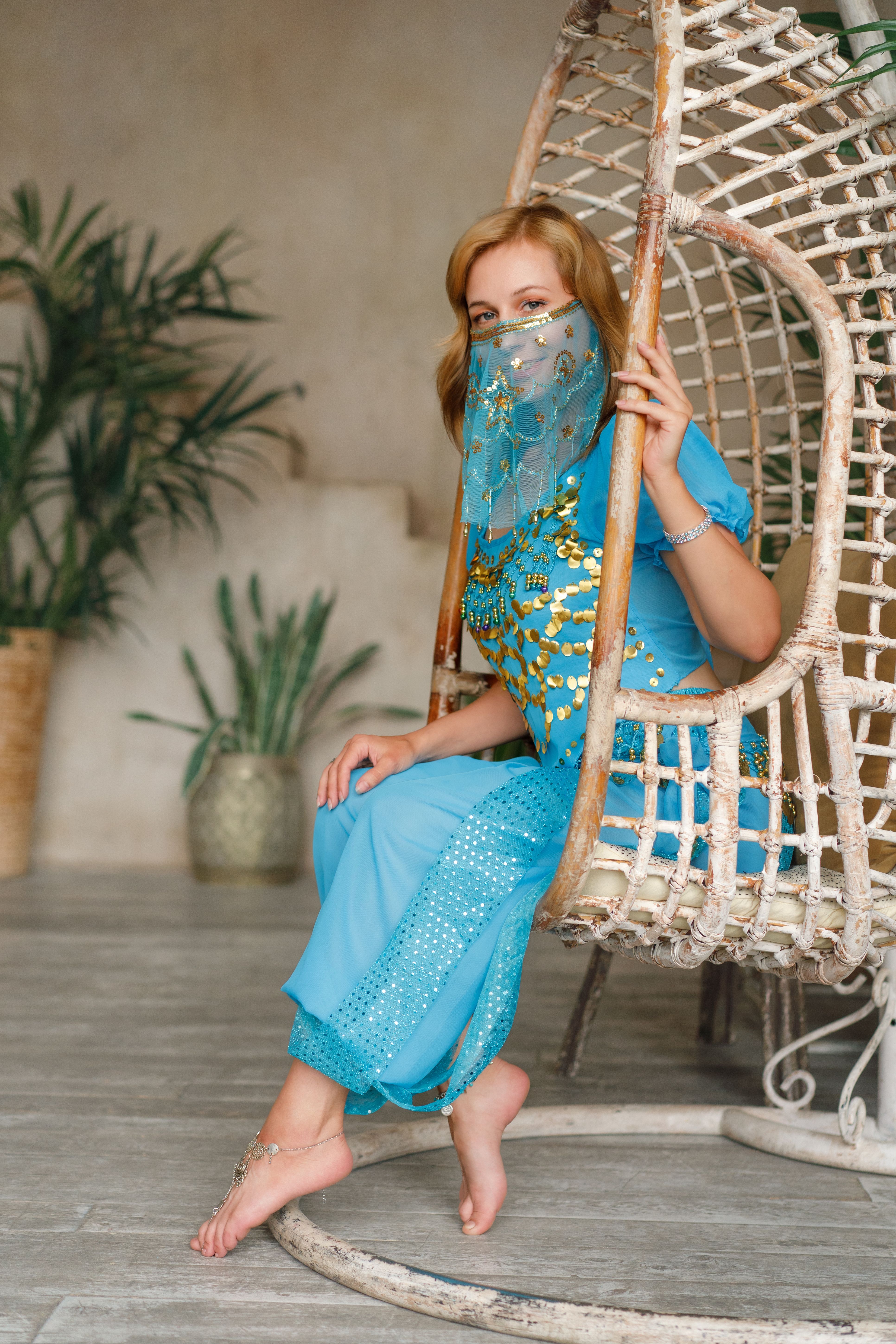 Caucasian woman in traditional attire sitting in a hanging chair, indoors.