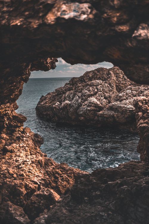 Free Dramatic coastal scene viewed through a rocky archway framing the ocean. Stock Photo