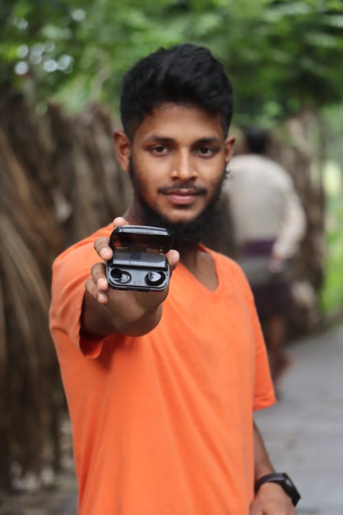 A Man in Orange Shirt Holding a Wireless Earbuds on the Case