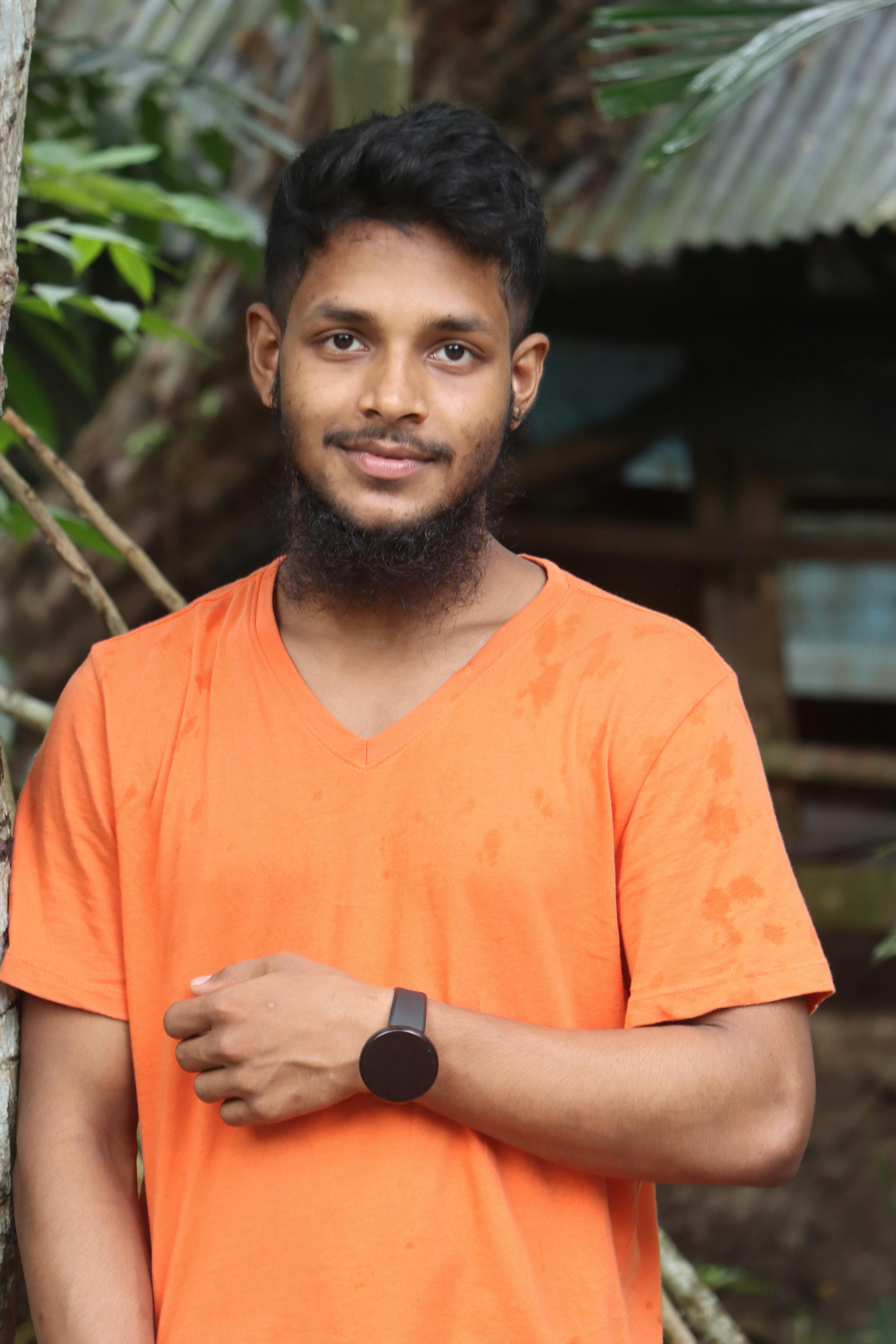 Young man in orange shirt smiling outdoors, showcasing joy and style.