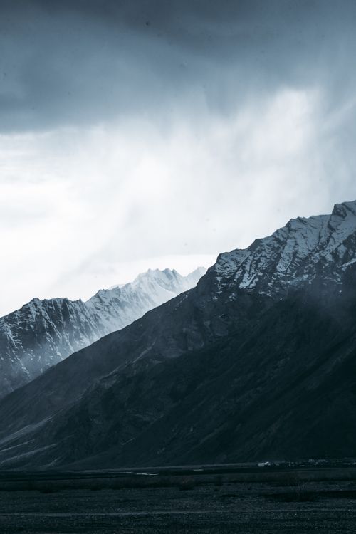 Free Majestic snow-capped mountains beneath a cloudy sky create a dramatic and scenic vista. Stock Photo