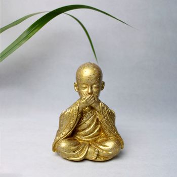 A serene golden monk statue in meditation with a green leaf backdrop, embodying peace and spirituality.