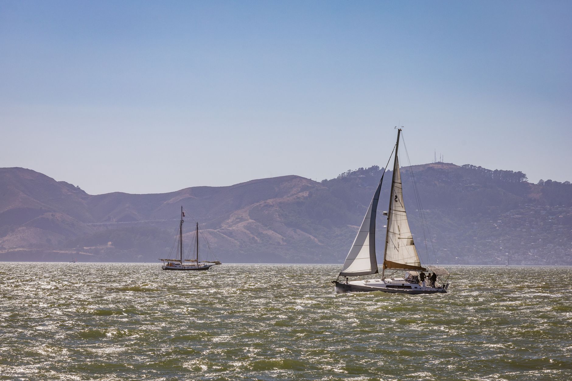 Sailboats navigates the shimmering waters near mountains, perfect for travel and adventure themes.