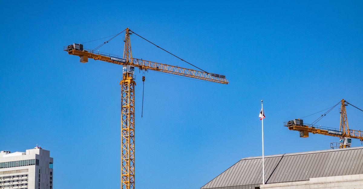Tower cranes against a clear blue sky at an urban construction site.